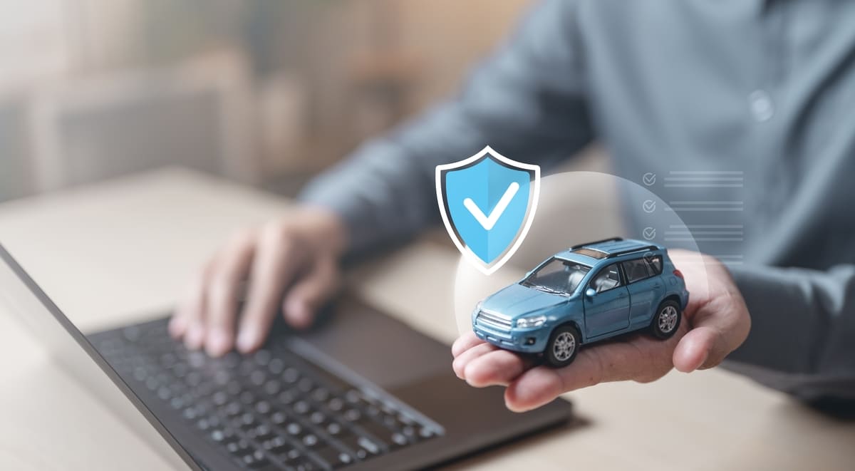 Kohustuslik liikluskindlustus - mehe käed arvuti ja mullis oleva mudelauto juures